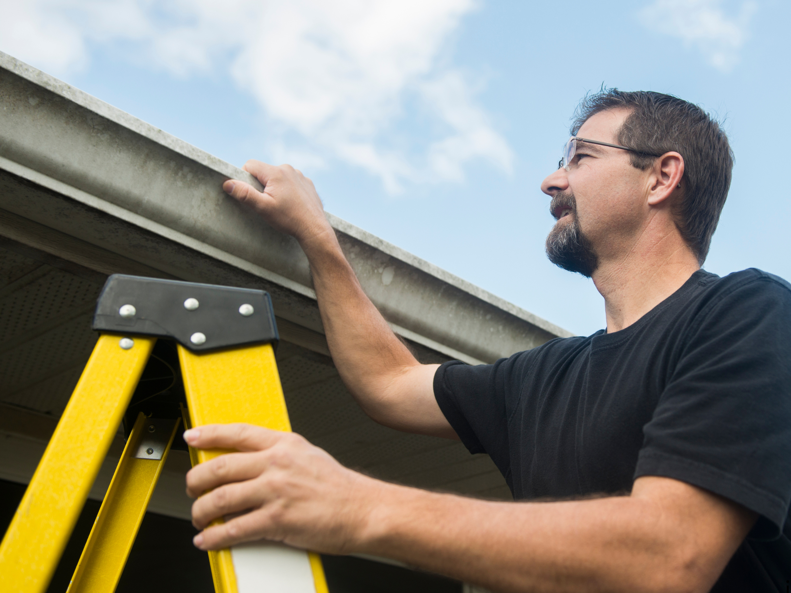 man with ladder looking into roof gutters